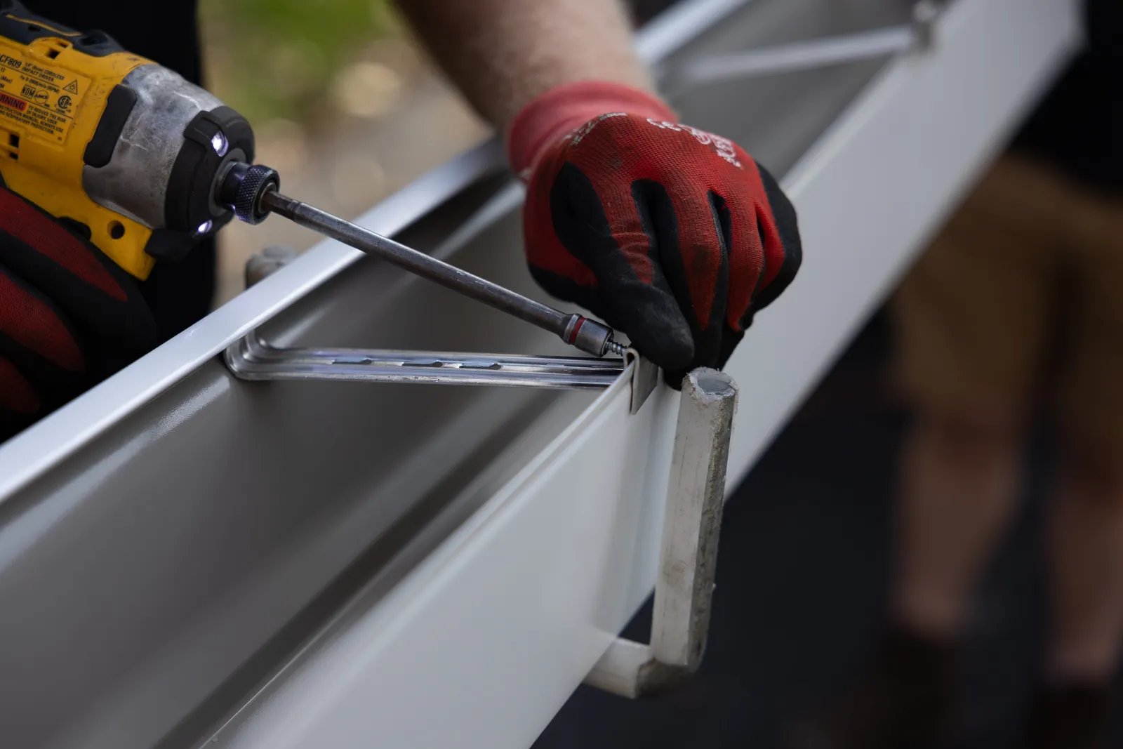 LeafFilter installer in red gloves fastening a gutter hanger with a power drill