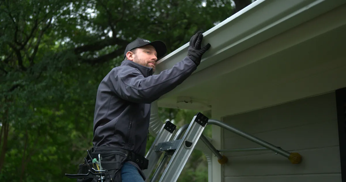 LeafFilter installer on a ladder reinforcing and aligning a home's gutters