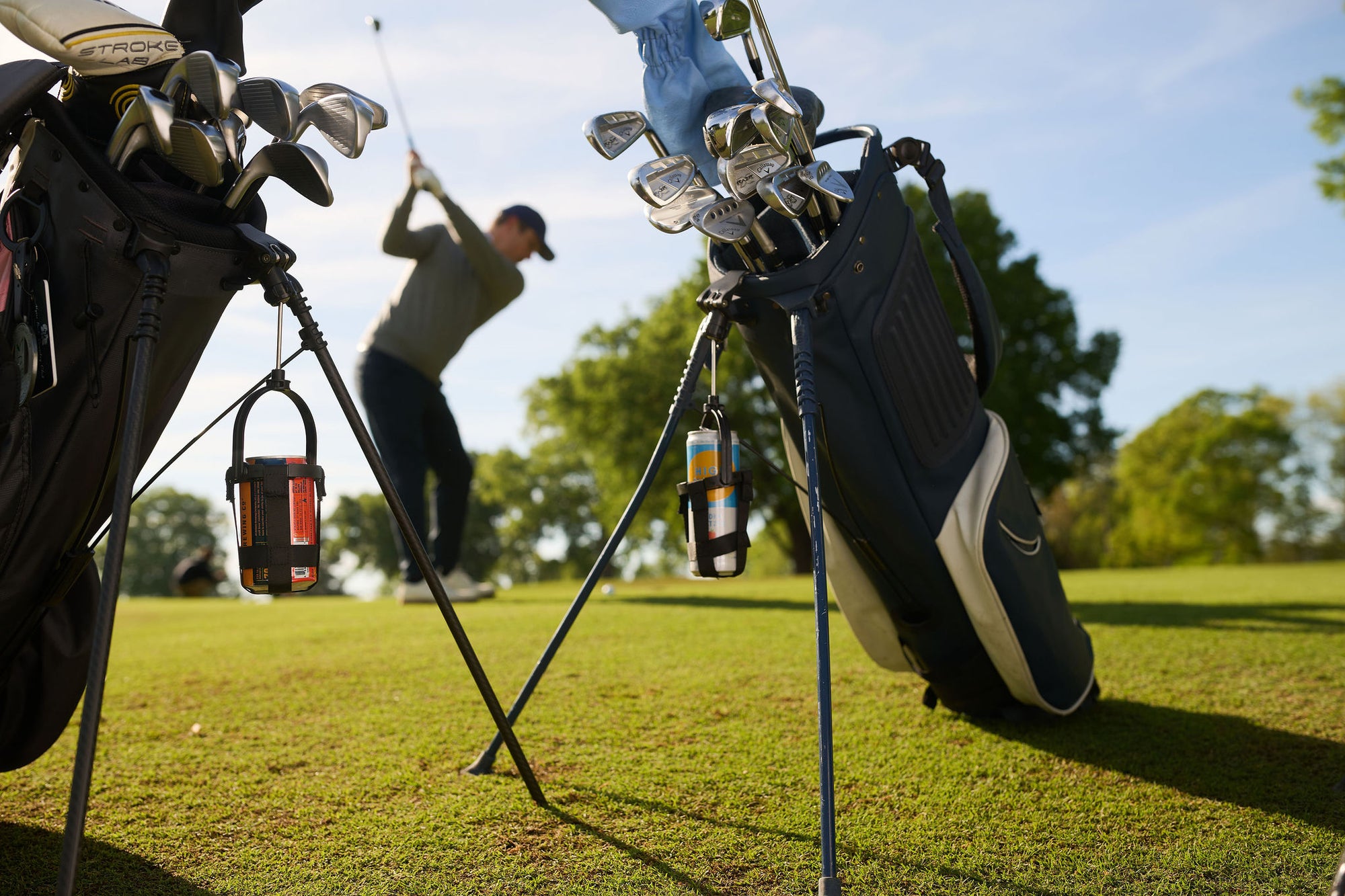 Golf bags with Dangler holders attached in the foreground, a golfer mid-swing behind them.