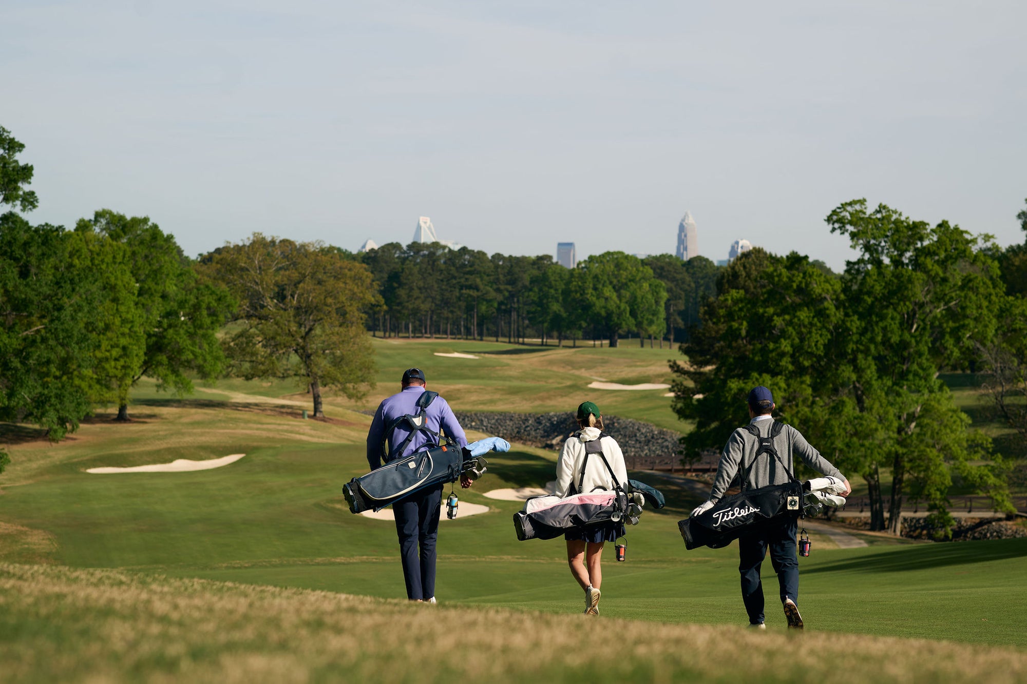 Three golfers walking a fairway with carry bags in early morning light.
