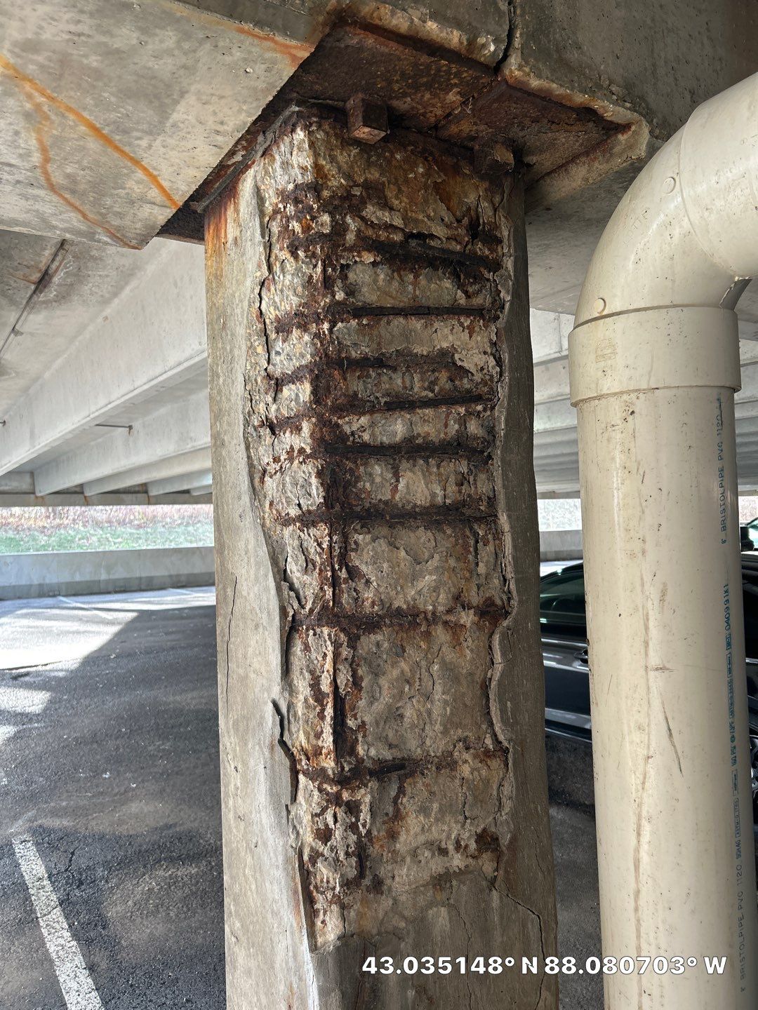 Severe concrete spalling on a reinforced parking garage column with exposed corroded rebar, showing extensive delamination from freeze-thaw cycling