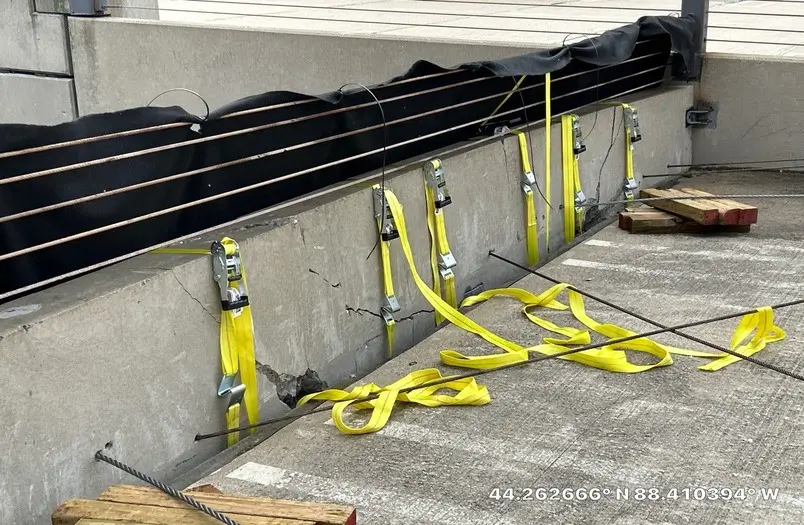 Emergency shoring system with yellow ratchet straps securing damaged 27,000-pound precast barrier panel at Appleton parking structure
