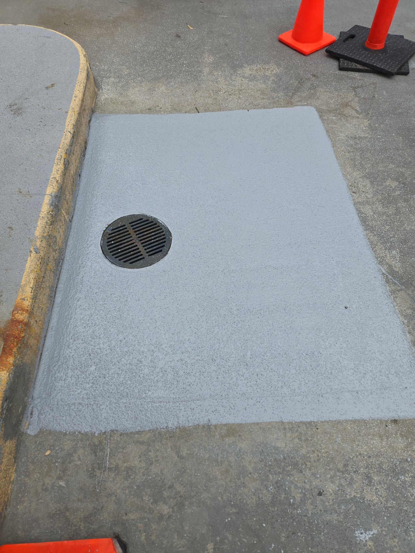 Completed drain repair with fresh gray traffic coating applied around a circular drain grate in a commercial underground parking ramp in Milwaukee, WI