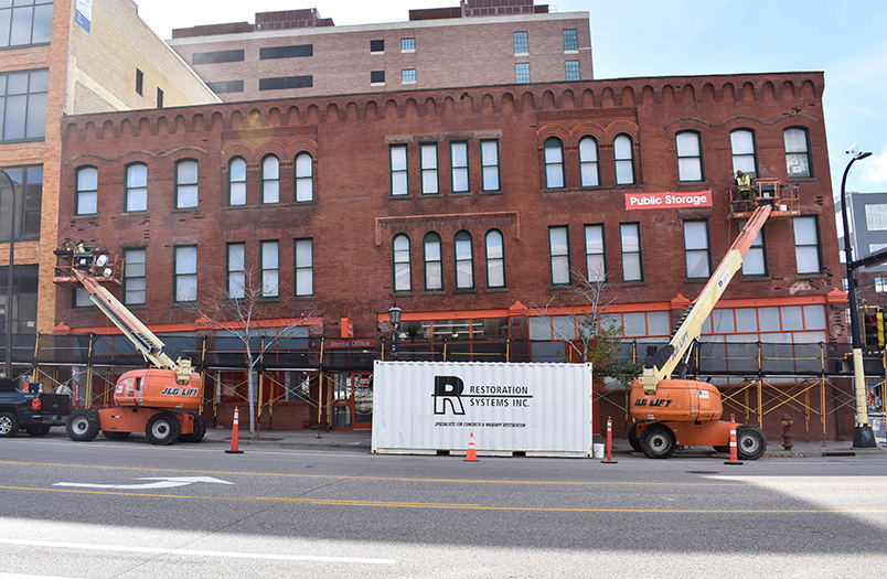 Brick building facade undergoing restoration with lift access equipment positioned at street level