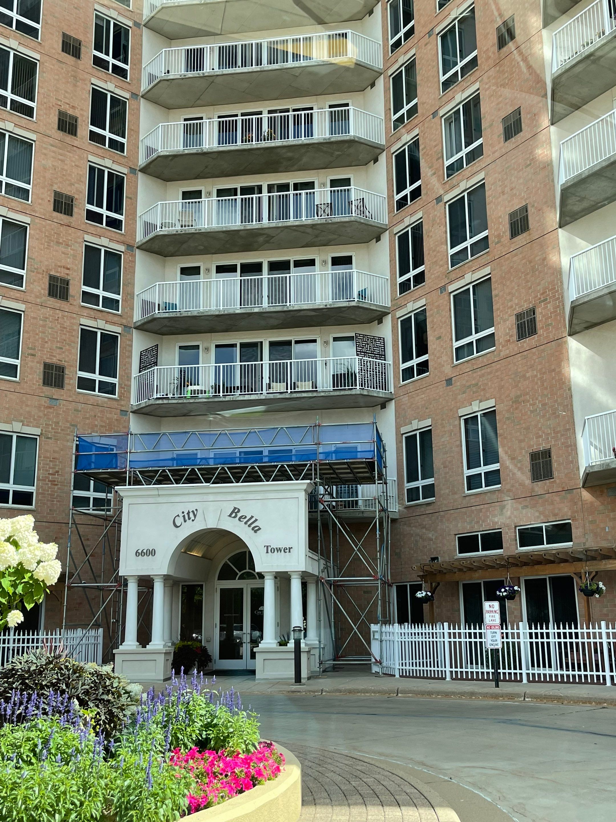 Condominium tower entrance with a white columned portico beneath a multi-story brick residential building with scaffolding