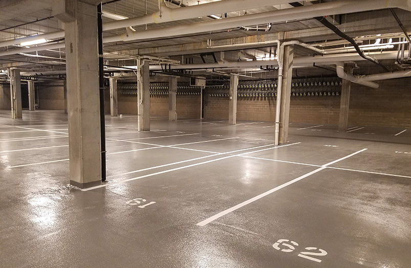 Interior of an empty concrete parking garage with numbered spaces, white support columns, and industrial ceiling infrastructure