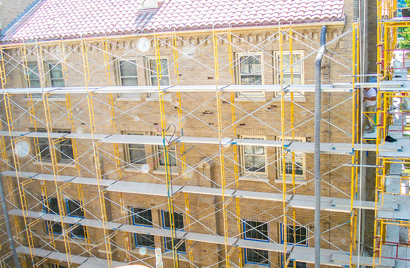 Brick wall under renovation with yellow metal scaffolding and safety netting surrounding masonry repair work