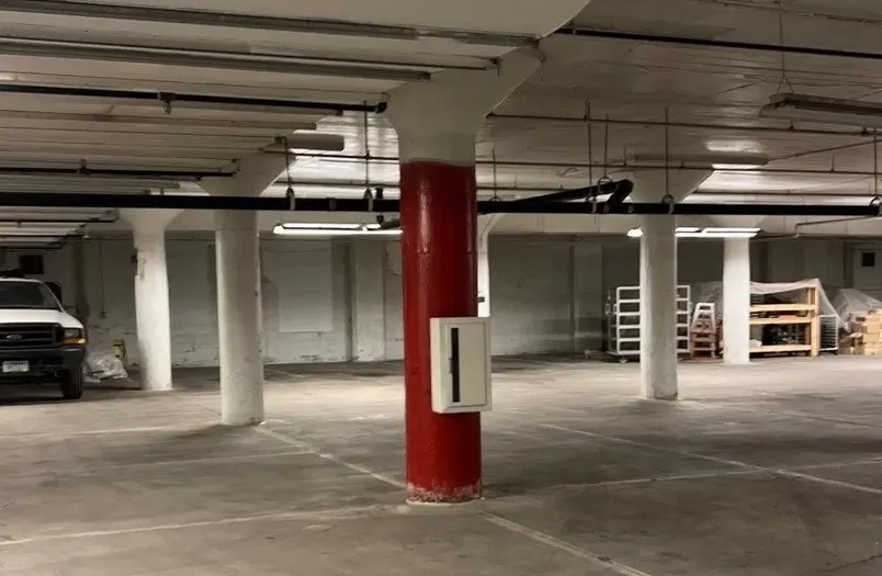 Worker in a yellow safety vest operating equipment on a concrete parking structure floor with metal floor inserts visible