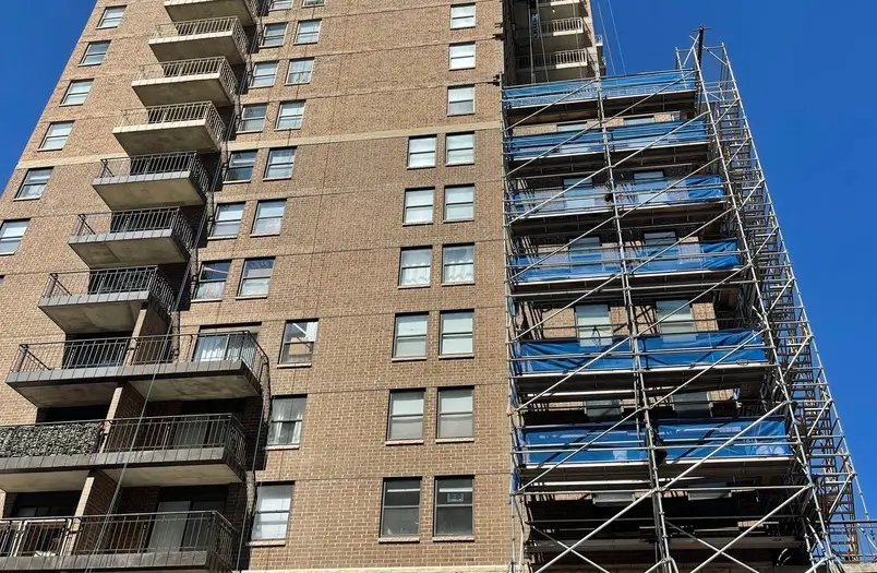 Brick commercial building with metal balconies beside construction scaffolding under a clear sky