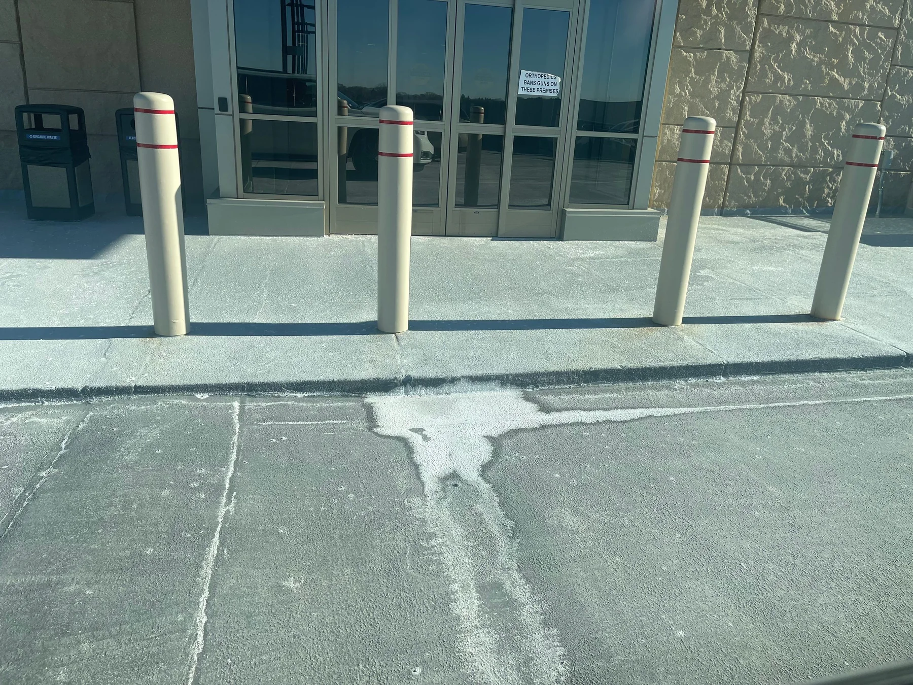 Surface-mounted steel bollards installed at a commercial building entrance, with deicing salt residue visible on the adjacent concrete walkway