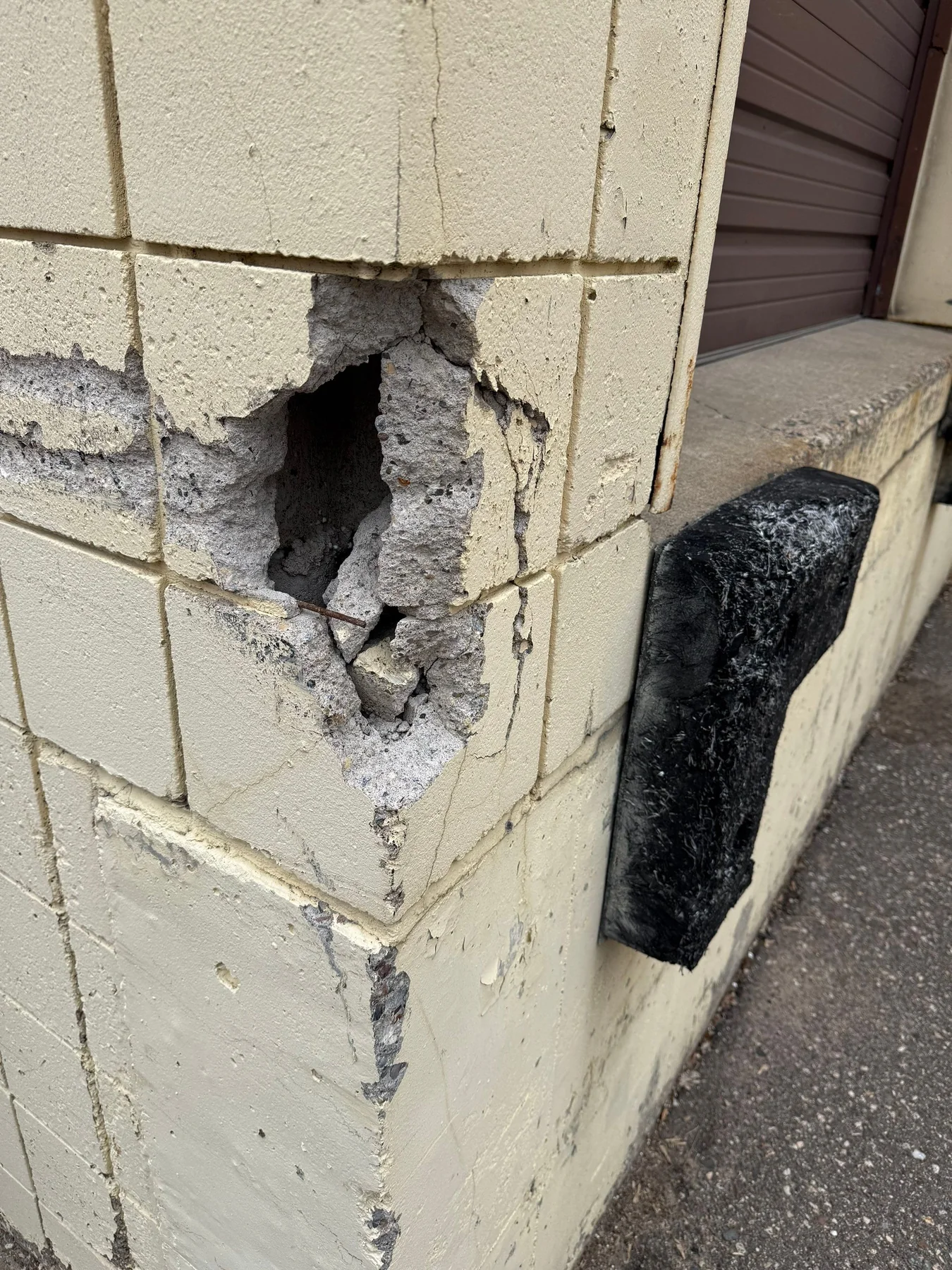 Spalled CMU masonry showing exposed aggregate and a failed paint coating - the kind of substrate that has to be repaired before any new coating can be applied