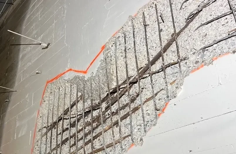 Exposed concrete with corroded rebar outlined in orange paint during an RSI leak investigation - the chloride-driven steel expansion that opened the leak path is fully visible