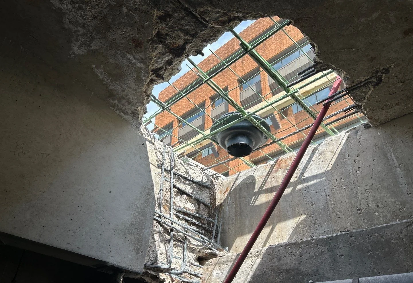 Open parking deck drain penetration viewed from below during clogged drain repair investigation