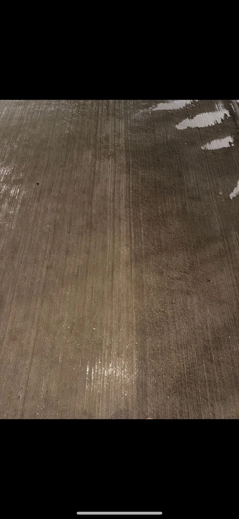 Close-up of a wet, freshly cleaned parking-deck concrete surface showing the contrast between scrubbed concrete and remaining residue, after high pressure hot water cleaning