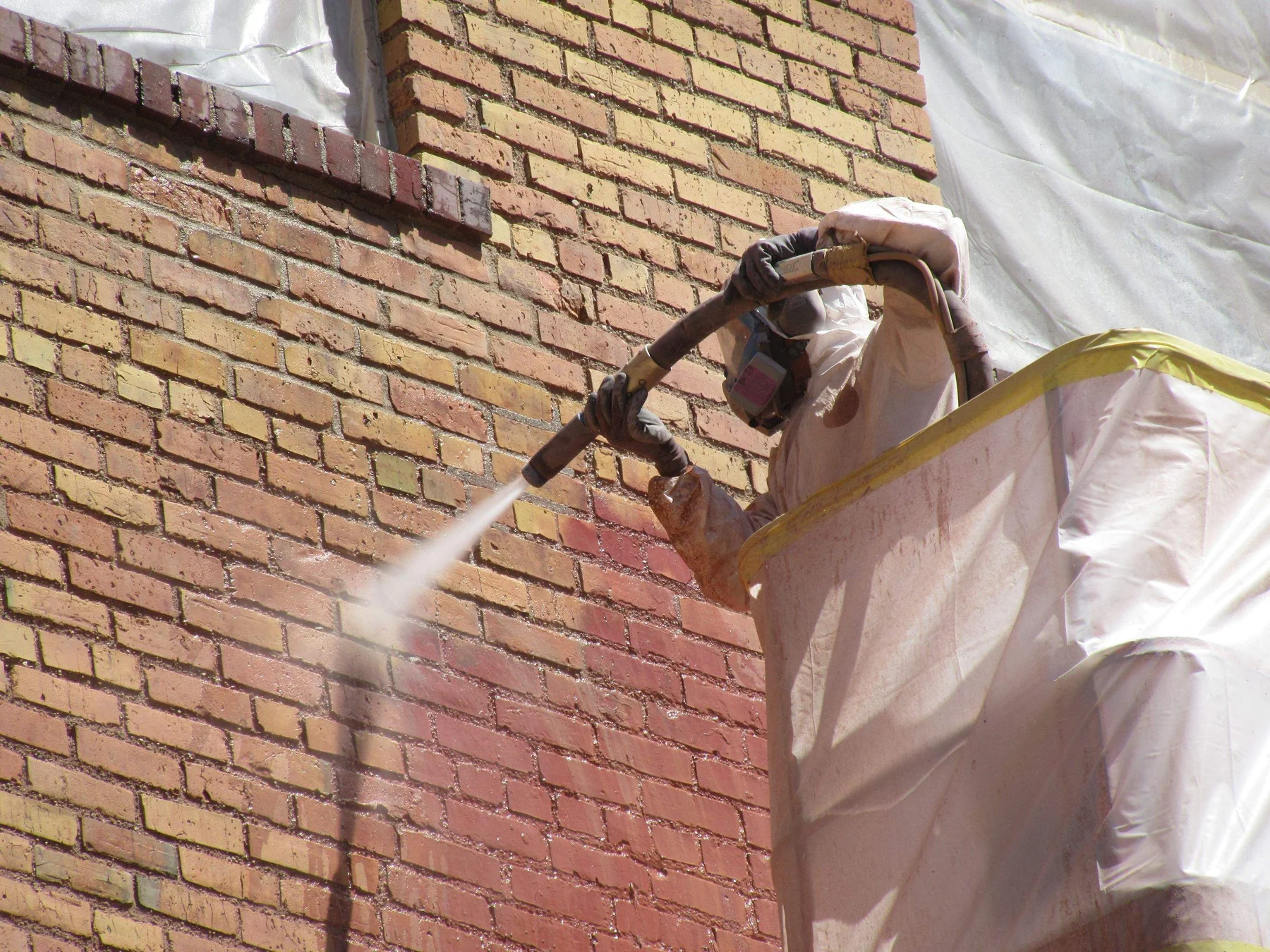 RSI technician in respirator and protective suit blasting failed paint off a brick masonry wall on a Minneapolis exterior restoration project