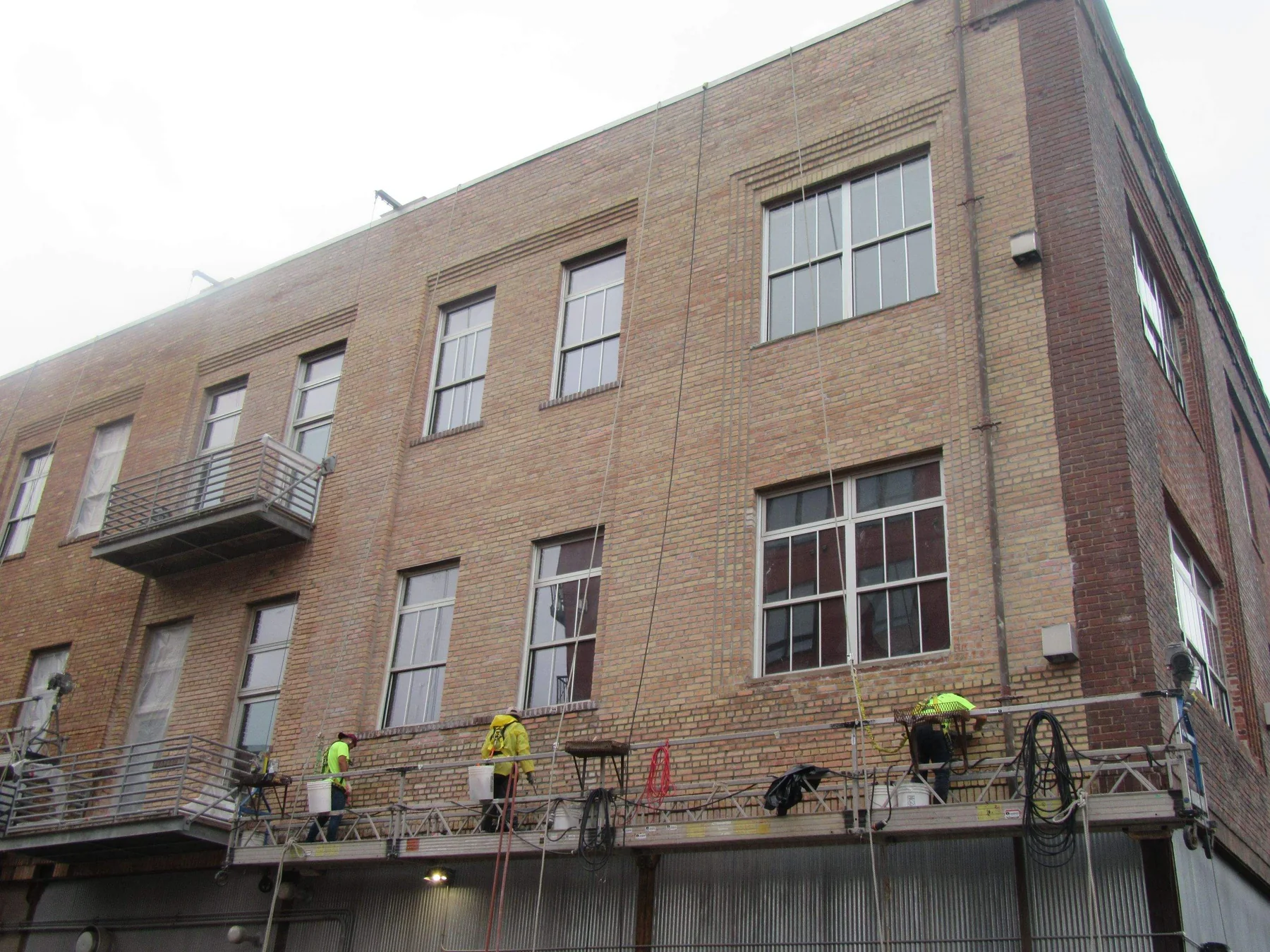 Technicians on a swing stage performing commercial paint removal and coating stripping on a masonry facade