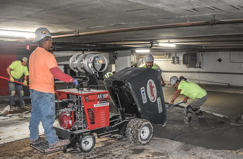 RSI crew placing fresh structural repair concrete on a parking deck floor with a riding-power buggy and finishing tools